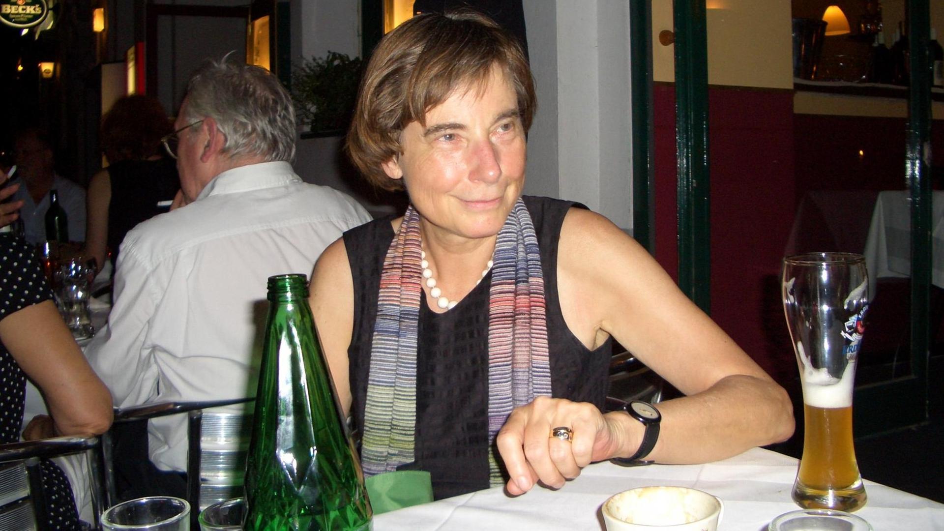 Claudia Schmölders sitzt in einem Restaurant, auf dem Tisch steht Wasser, Weizenbier und Kaffee.
