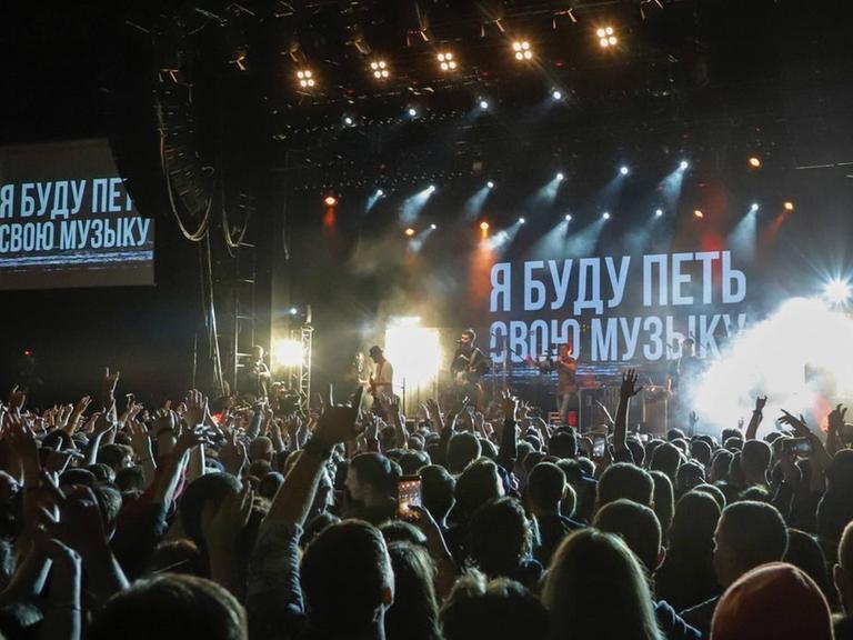 Im Hintergrund eine Bühne mit russischer Schrift. Davor eine Zuschauermenge.