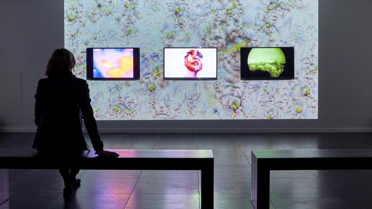 Eine Besucherin sitzt vor der aus drei Bildern bestehenden Installation Eine Besucherin sitzt vor der aus drei Bildern bestehenden Installation