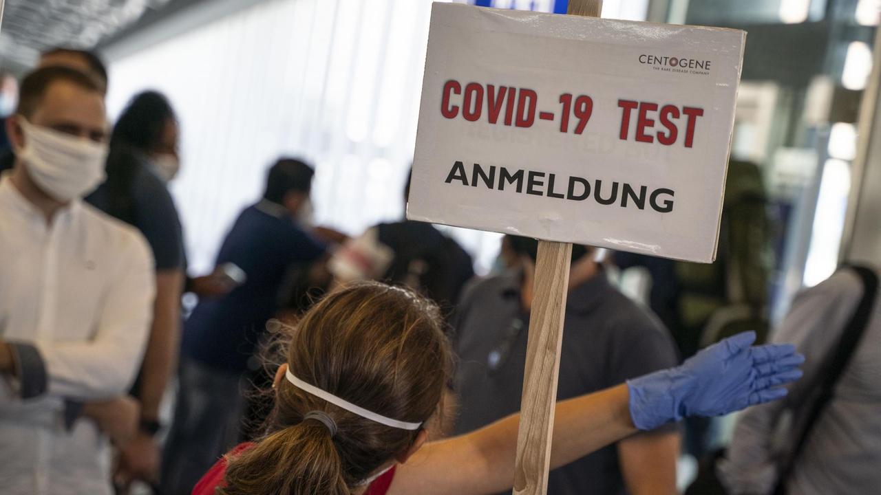 Eine Bedienstete weist in einem Terminal des Frankfurter Flughafens den Weg zur Anmeldung für einen Corona-Test. Eine Bedienstete weist in einem Terminal des Frankfurter Flughafens den Weg zur Anmeldung für einen Corona-Test.