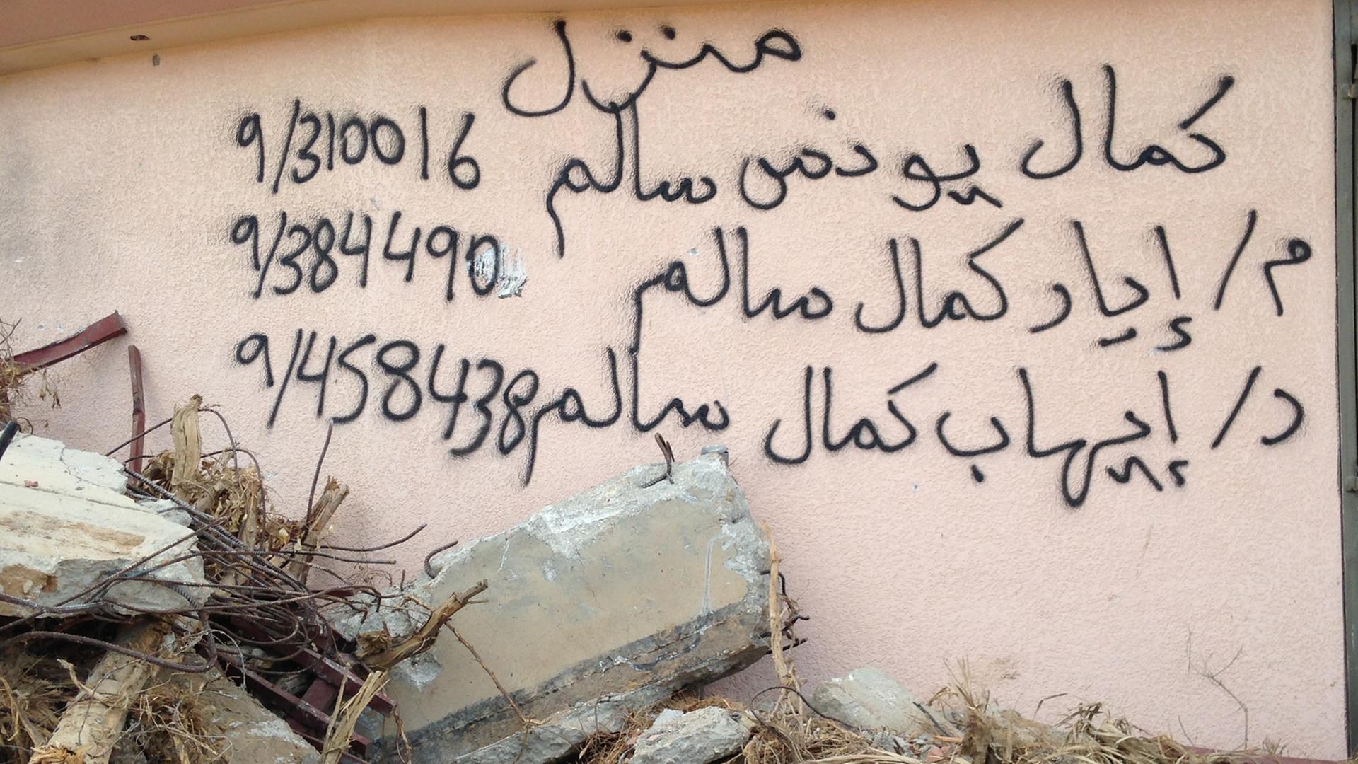 Arabische Schriftzeichen und Zahlen stehen auf auf einer Hauswand, davor liegen Steine und Trümmer Arabische Schriftzeichen und Zahlen stehen auf auf einer Hauswand, davor liegen Steine und Trümmer