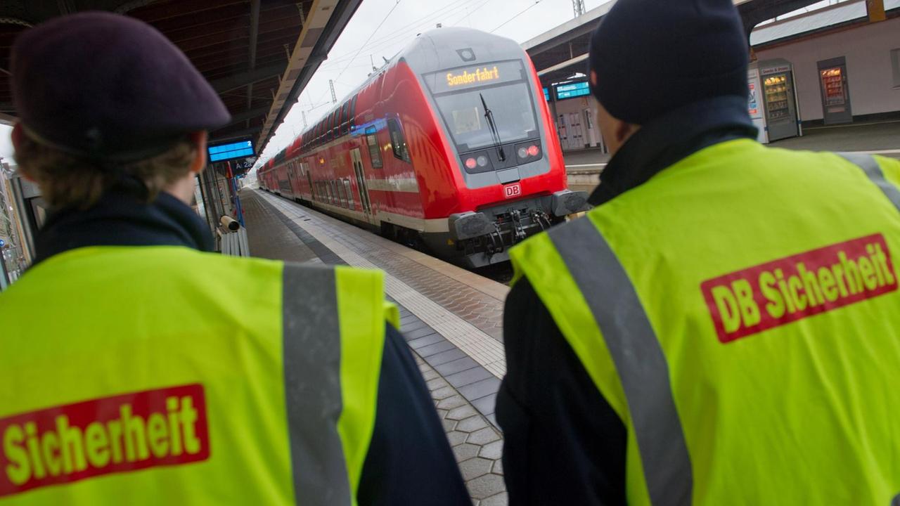 Im Vordergrund sieht man zwei Mitarbeiter des Sicherheitspersonals der Deutschen Bahn. Im Hintergrund eine Regionalbahn RE 5 im Bahnhof von Stralsund (Mecklenburg-Vorpommern). Im Vordergrund sieht man zwei Mitarbeiter des Sicherheitspersonals der Deutschen Bahn. Im Hintergrund eine Regionalbahn RE 5 im Bahnhof von Stralsund (Mecklenburg-Vorpommern).