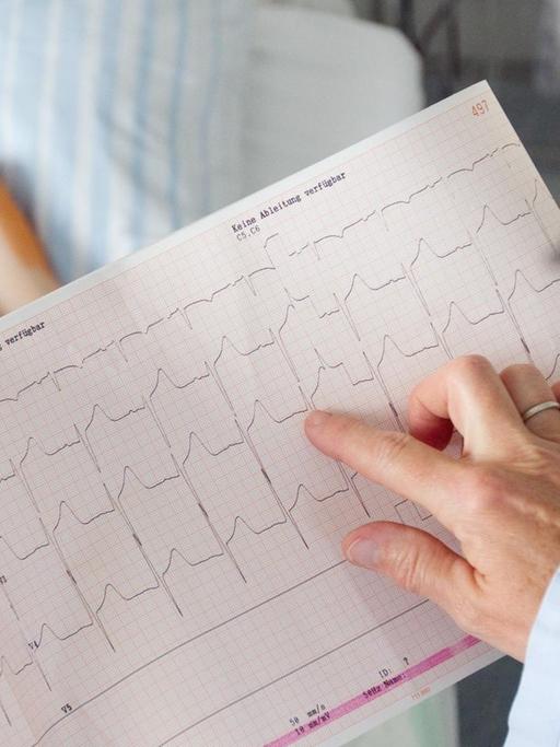 Ein am Herzen operierter Junge liegt auf der Intensivstation der Kinderkardiologie im Universitätsklinikum Münster (UKM) in einem Bett, während eine Medizinisch-technische Assistentin, den Ausdruck von einem Elektrokardiogramm (EKG) auswertet.