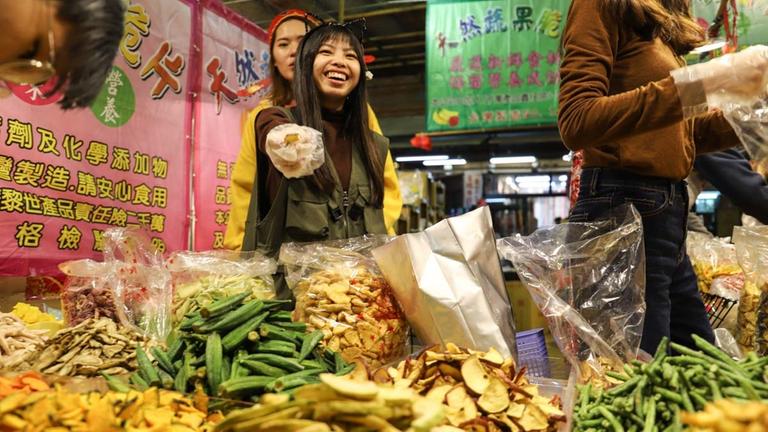 Eine Frau präsentiert die Waren auf einem Stand des Nachtmarktes in Taipeh Eine Frau präsentiert die Waren auf einem Stand des Nachtmarktes in Taipeh
