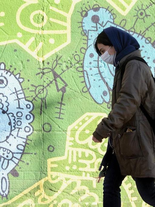 Frau mit Mund-Nasen-Schutz geht durch Teheran.