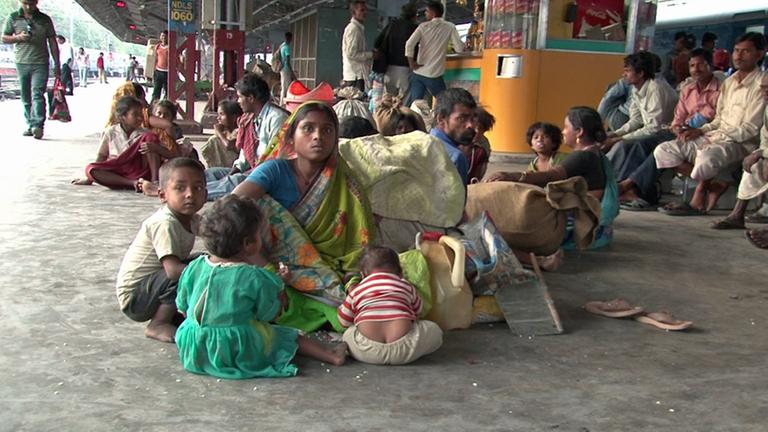 Kinder sitzen um ihre Mutter auf dem Boden eines Bahnsteiges in Neu-Delhi. Sie tragen keine Schuhe.