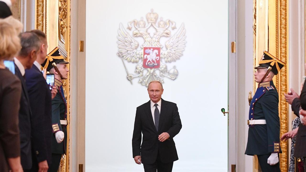 Der russische Präsident Wladimir Putin schreitet im Kreml auf einem roten Teppich einen Saal mit Gästen ab.