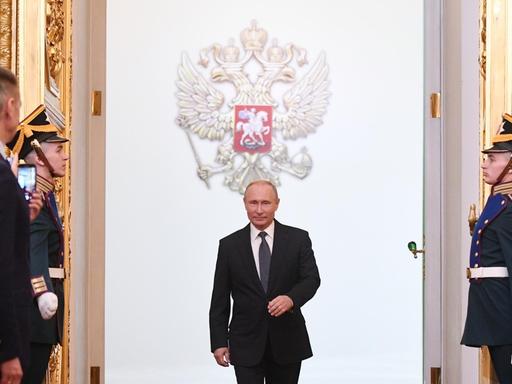 Der russische Präsident Wladimir Putin schreitet im Kreml auf einem roten Teppich einen Saal mit Gästen ab.