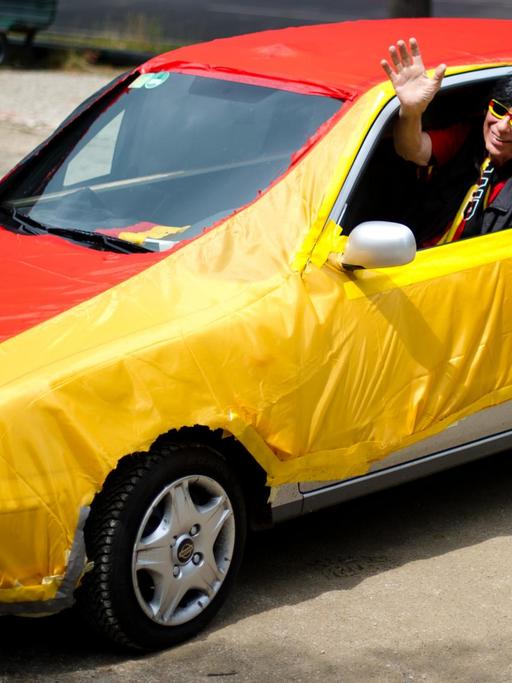 Ein Jogi-Löw-Double in einem Auto, das in eine Deutschlandfahne gehüllt ist