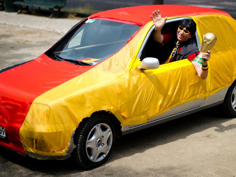 Ein Jogi-Löw-Double in einem Auto, das in eine Deutschlandfahne gehüllt ist