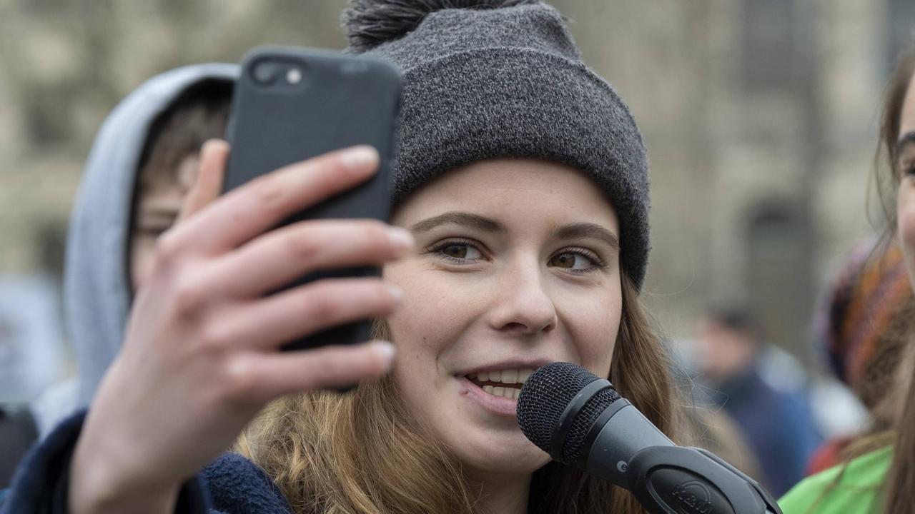 Klimaaktivistin Luisa Neubauer spricht beim freitäglichen Schülerstreik in Berlin in ein Mikrofon und hält dabei ein Handy hoch