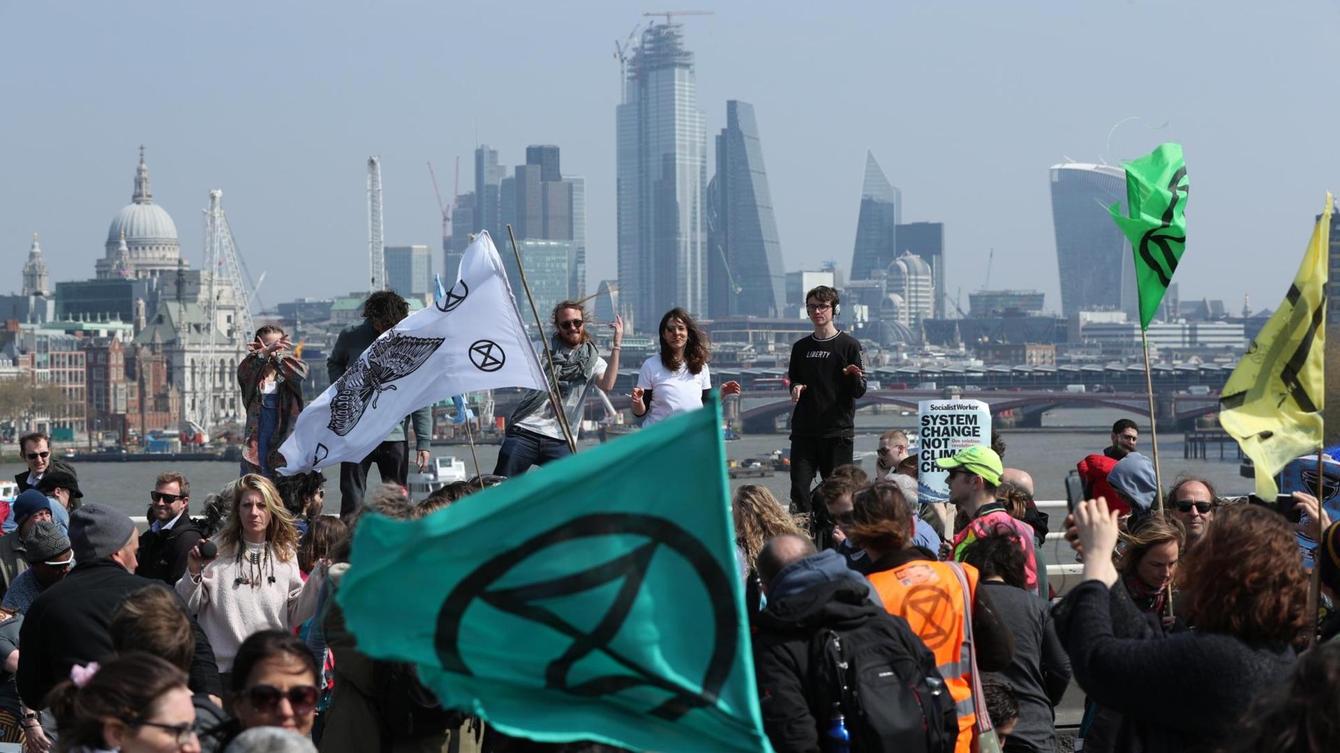 Demonstranten protestieren auf der Waterloo Bridge für den Klimaschutz. Im Hintergrund sieht man die Skyline von London.