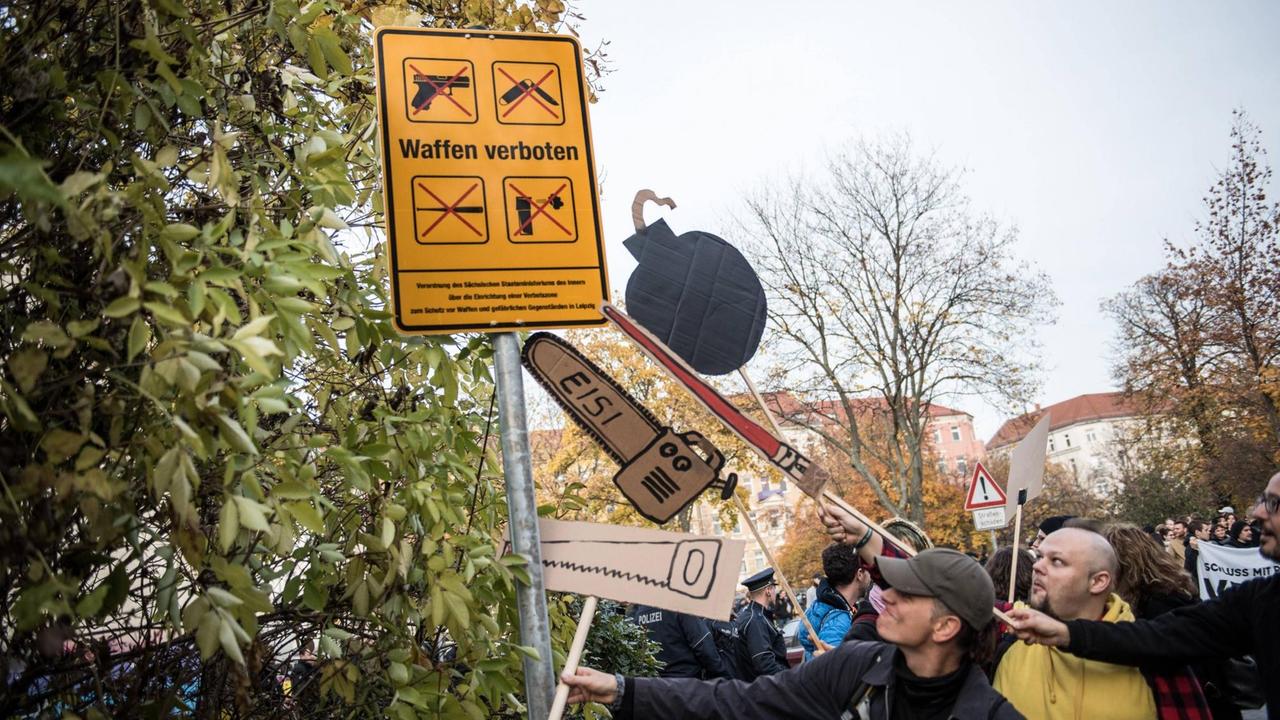 Symbolisch sägen Demonstranten mit ihren, aus Pappe gebastelten, Bomben und Sägen an dem neu aufgestellten Schild mit der Aufschrift "Waffen verboten".