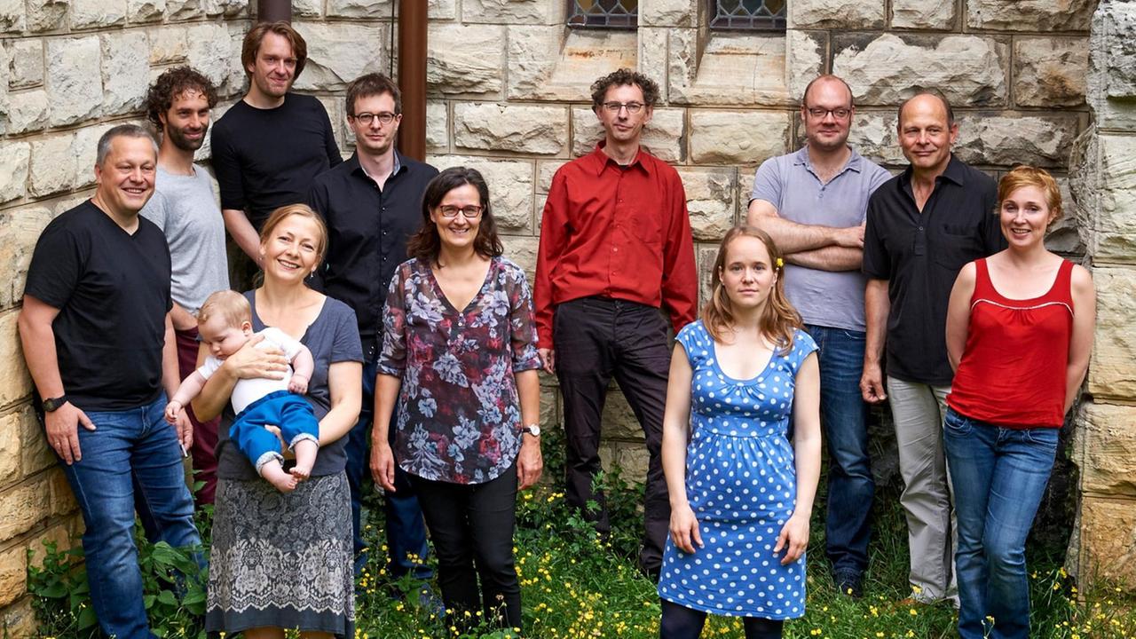Elf Mitglieder, Frauen wie Männer des Berlin Athesinus Consorts stehen auf einer Wiese vor einem historischen Gemäuer in Alltagskleidung und schauen entspannt in die Kamera, wobei eine Frau ein kleines Kind auf dem Arm hält. Elf Mitglieder, Frauen wie Männer des Berlin Athesinus Consorts stehen auf einer Wiese vor einem historischen Gemäuer in Alltagskleidung und schauen entspannt in die Kamera, wobei eine Frau ein kleines Kind auf dem Arm hält.