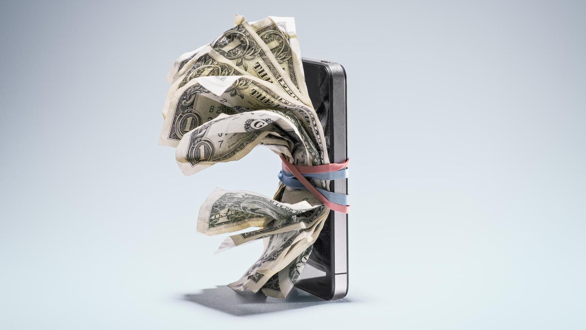 Illustration für eine bargeldlose Gesellschaft: Zerknitterte Dollarscheine sind mit Gummibändern an einem Smartphone befestigt.