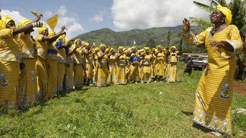 Frauen nehme am "Christian Women's Fellowship" in Kamerun teil. Sie tragen gelbe Gewänder, die Leiterin der Gruppe steht vor ihnen und gibt Handzeichen.