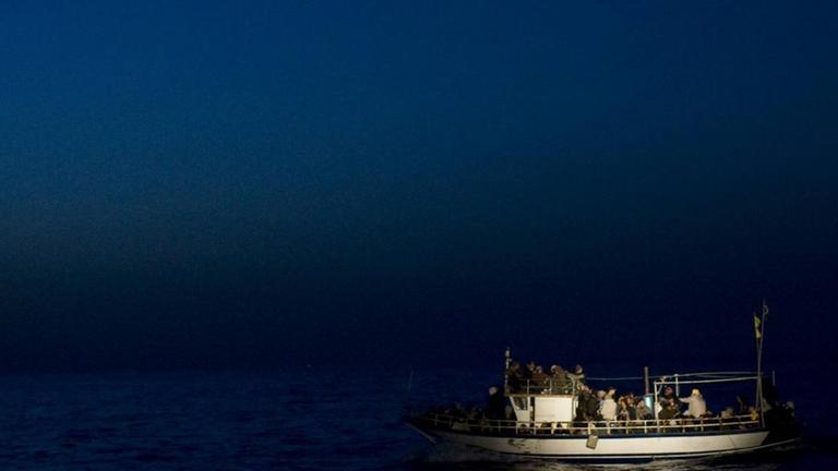Ein kleines Boot mit vielen Menschen liegt auf dem Wasser. Es ist Nacht, das Boot wird angestrahlt. Ein kleines Boot mit vielen Menschen liegt auf dem Wasser. Es ist Nacht, das Boot wird angestrahlt.