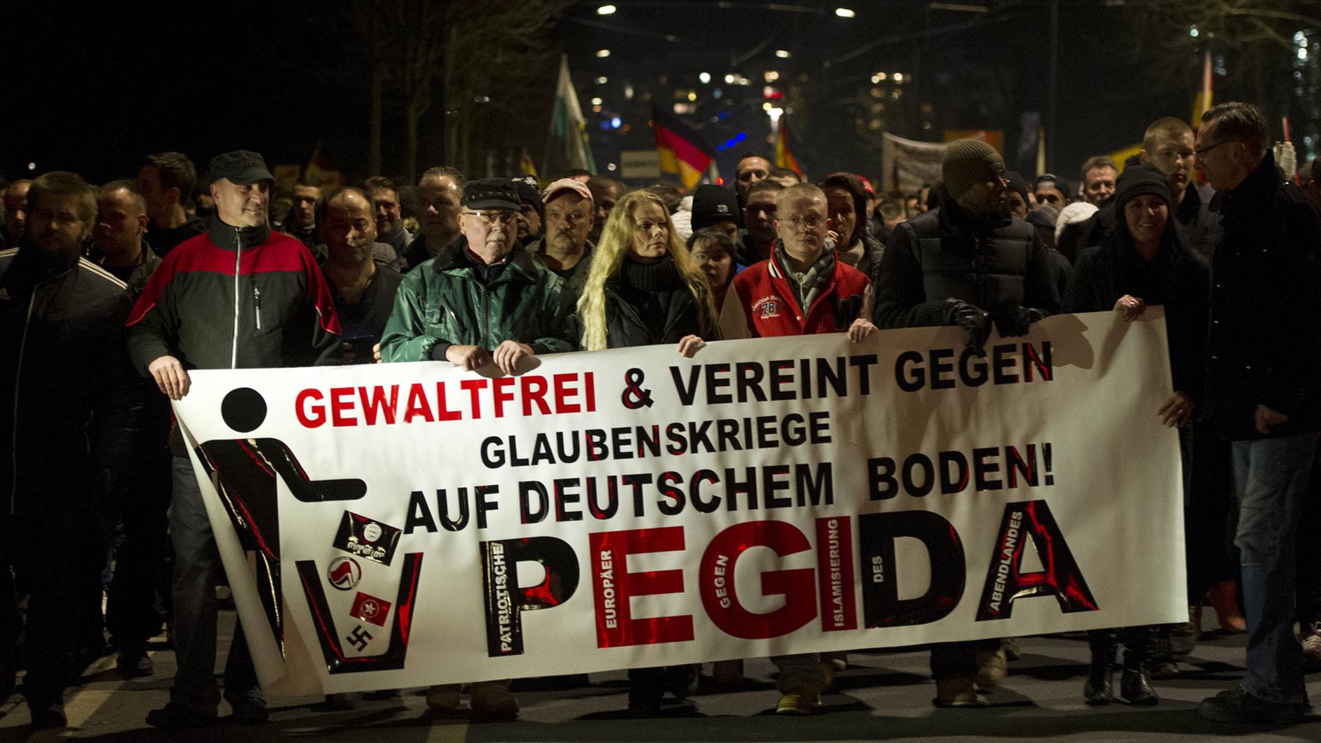Mehrere Pegida-Demonstranten halten ein Banner mit der Aufschrift "Gewaltfrei und vereint gegen Glaubenskriege auf deutschem Boden!" Mehrere Pegida-Demonstranten halten ein Banner mit der Aufschrift "Gewaltfrei und vereint gegen Glaubenskriege auf deutschem Boden!"