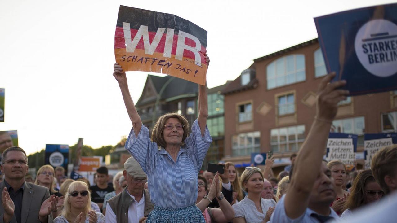 Teilnehmer einer Kundgebung der CDU zeigen ihren Zuspruch zu Merkels Migrationspolitik. Eine Frau hält ein Plakat mit ihrem Satz "Wir schaffen das" in die Höhe.