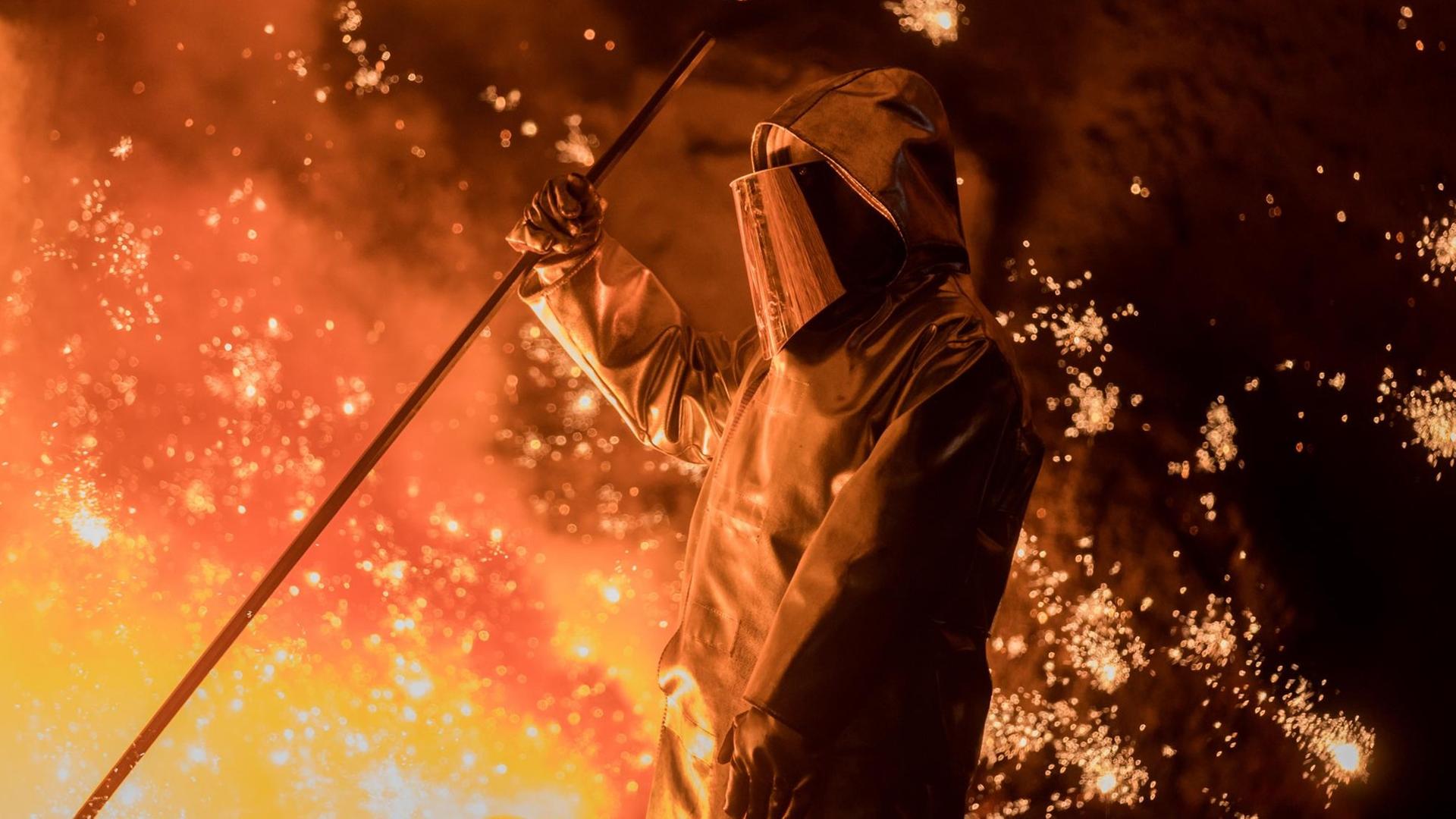 Ein Hochöfner bei der Arbeit - mit Schutzanzug inmitten von glühendem Stahl. Ein Hochöfner bei der Arbeit - mit Schutzanzug inmitten von glühendem Stahl.