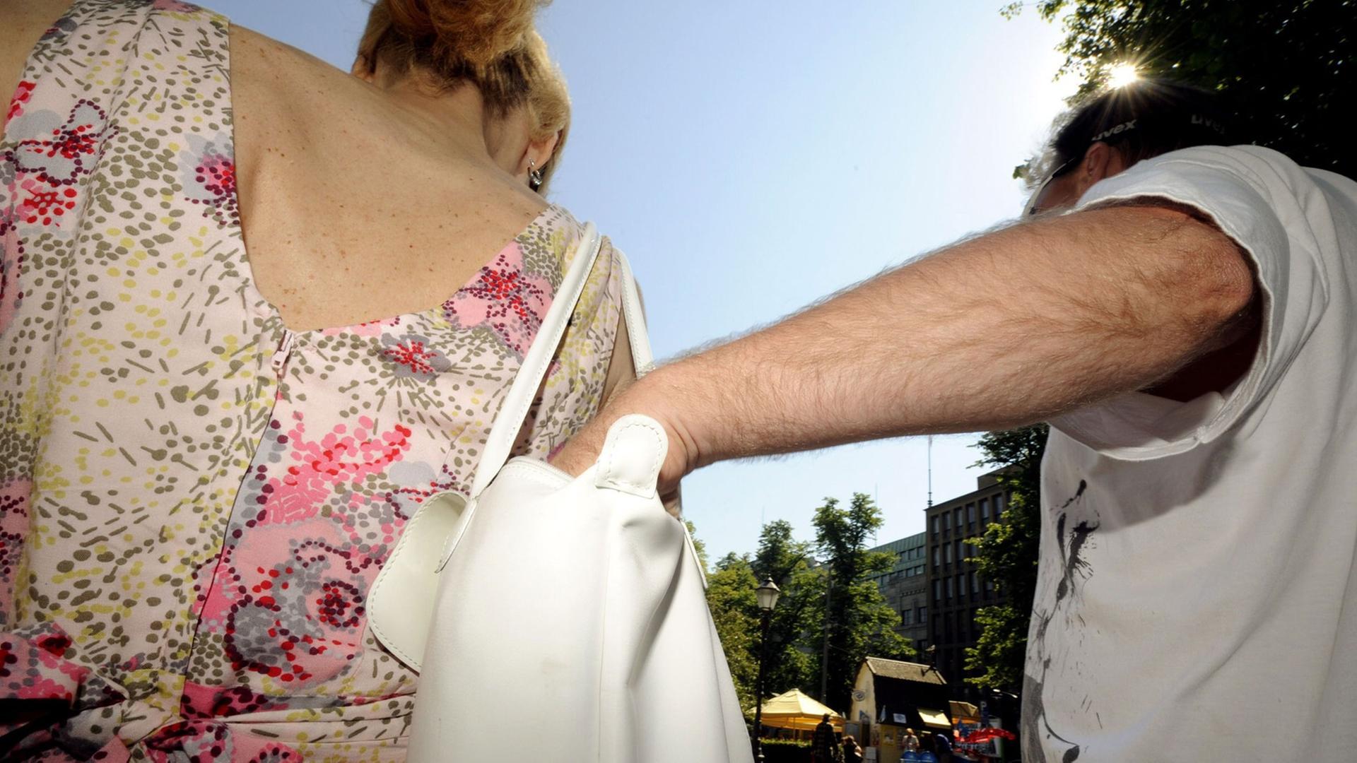 Ein Dieb steckt seine Hand in die Handtasche einer Frau