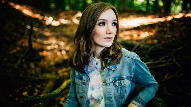Jazz-Sängerin Laura Totenhagen sitzt im Wald und schaut verträumt zur Seite.