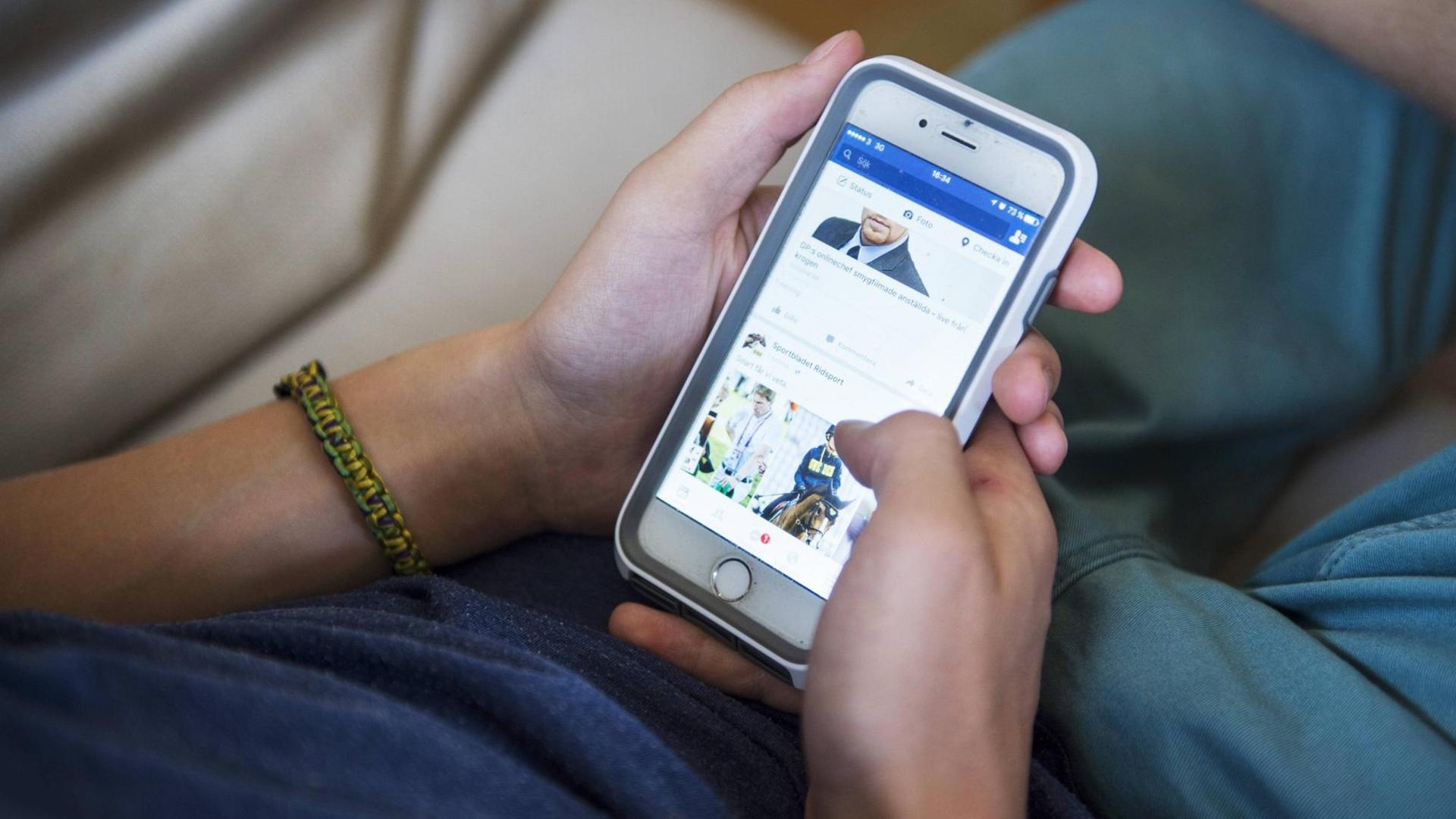 Ein Junge surft auf seinem Smartphone bei Facebook.