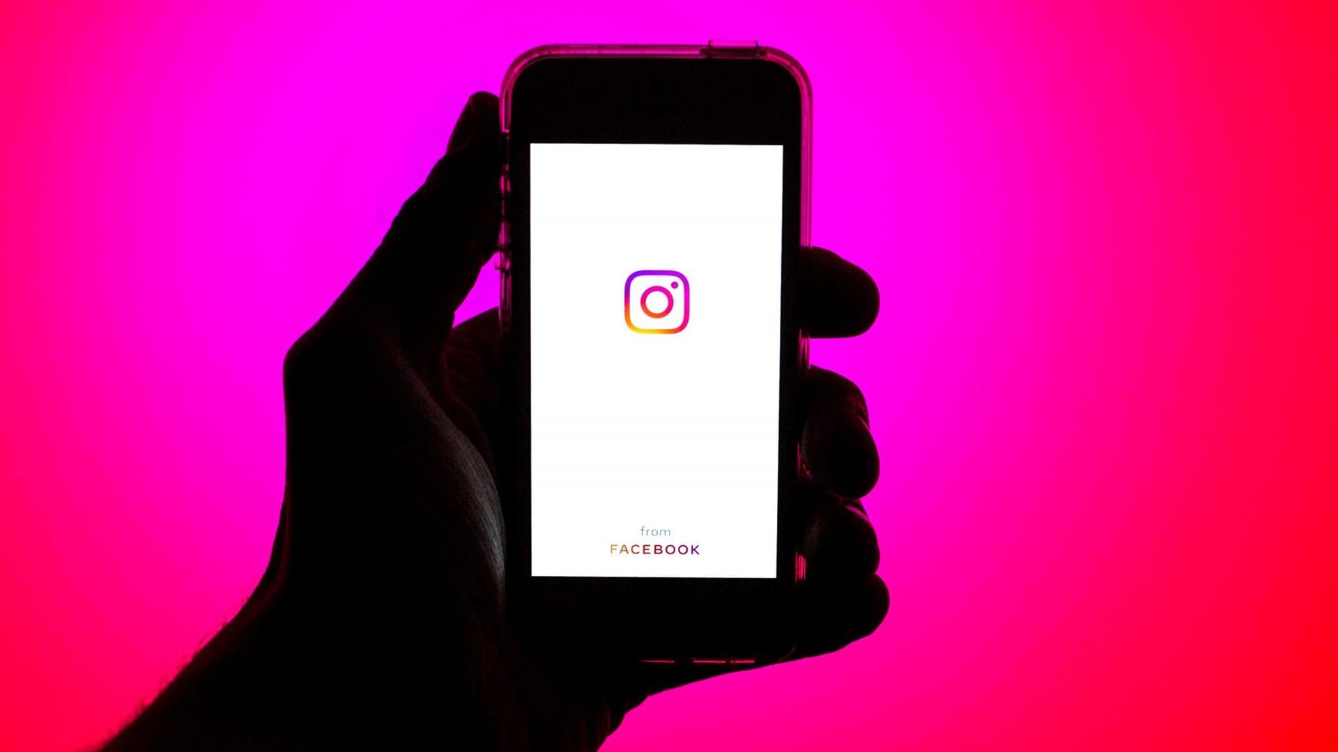 Eine Hand hält ein Smartphone mit dem Instagram Logo auf dem Bildschirm.