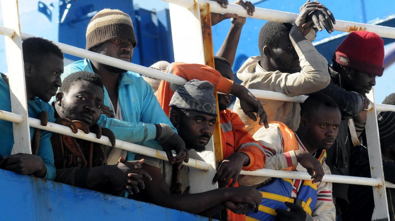 Flüchtlinge schauen auf einem Schiff durch die Stangen der Reeling Flüchtlinge schauen auf einem Schiff durch die Stangen der Reeling