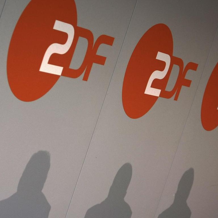Bei einer Pressekonferenz beim ZDF in Mainz werden die Schatten dreier Menschen an die Logo-Wand geworfen.
