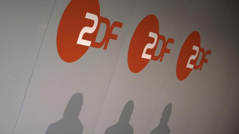 Bei einer Pressekonferenz beim ZDF in Mainz werden die Schatten dreier Menschen an die Logo-Wand geworfen.
