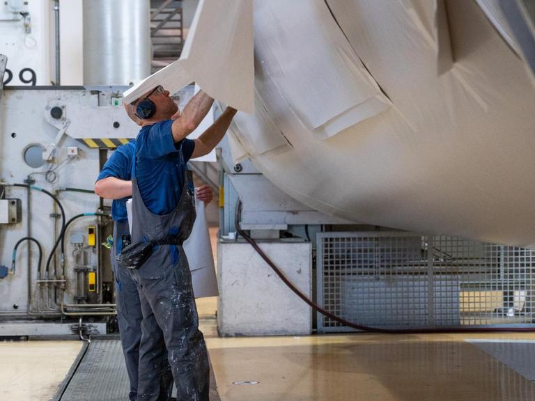 Zwei Arbeiter bearbeiten eine Papierrolle in der Papierfabrik des Herstellers Leipa in Schwedt/Oder.