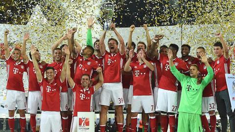 Die Mannschaft von Bayern München hält den Pokal im Gold-Regen hoch.