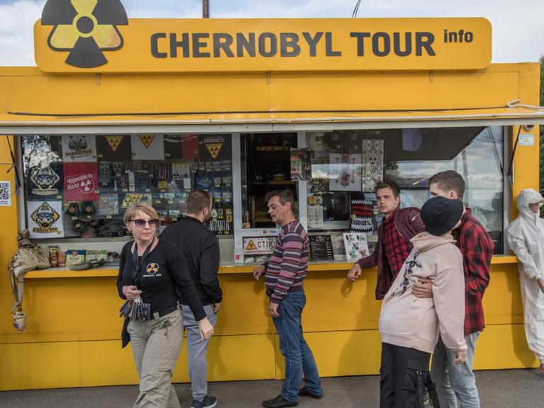 Ein Stand für Touristen im Gebiet des 1986 explodierten Atomkraftwerks Tschernobyl. Er ist gelb mit dem Atomenergie-Symbol. Einige Menschen stehen davor, um sich etwas zu kaufen.