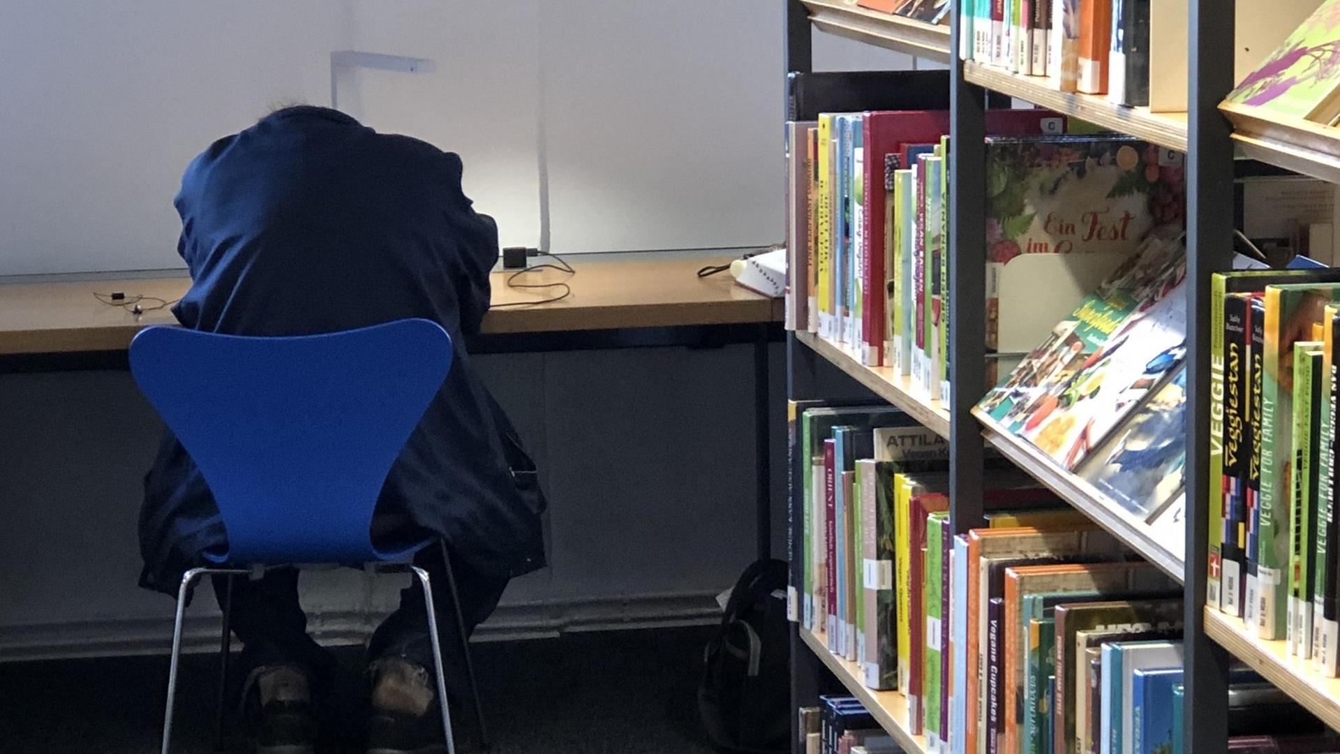 Ein Mann liegt mit dem Kopf auf dem Tisch einer Bibliothek. Ein Mann liegt mit dem Kopf auf dem Tisch einer Bibliothek.