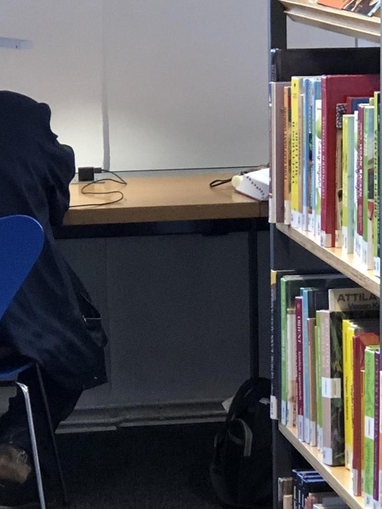 Ein Mann liegt mit dem Kopf auf dem Tisch einer Bibliothek.