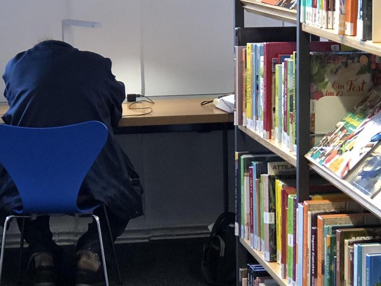 Ein Mann liegt mit dem Kopf auf dem Tisch einer Bibliothek.