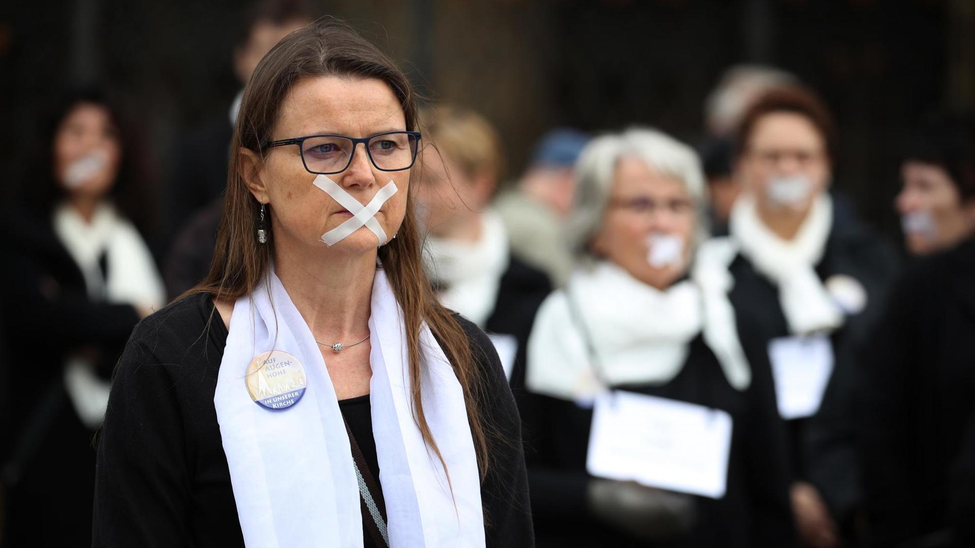 Das Foto zeigt einen Flasmob vor dem Ulmer Münster gegen die männlichen Machtstrukturen in der katholischen Kirche. Mehrere Frauen haben ihre Münder mit Klebestreifen zugeklebt. Das Foto zeigt einen Flasmob vor dem Ulmer Münster gegen die männlichen Machtstrukturen in der katholischen Kirche. Mehrere Frauen haben ihre Münder mit Klebestreifen zugeklebt.