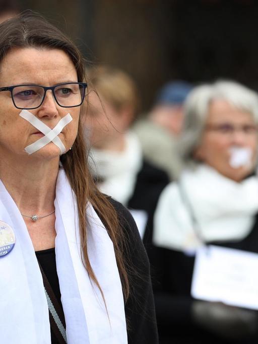 Das Foto zeigt einen Flasmob vor dem Ulmer Münster gegen die männlichen Machtstrukturen in der katholischen Kirche. Mehrere Frauen haben ihre Münder mit Klebestreifen zugeklebt.