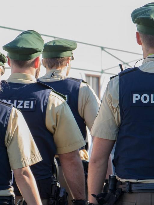 Sechs Polizisten in Zweierreihen von hinten, bekleidet mit Westen mit der Aufschrift "Polizei"