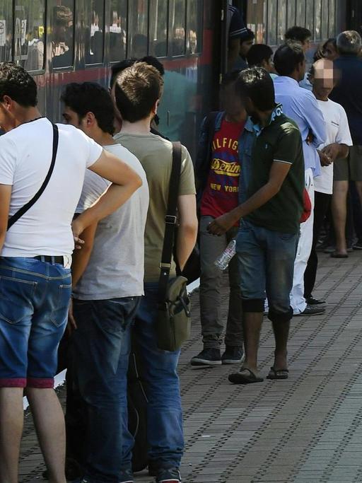Flüchtlinge stehen auf einem Bahnsteig an einem Zug.
