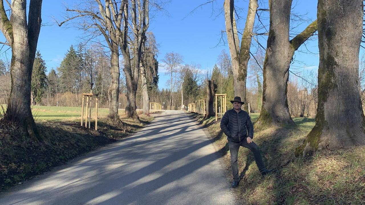 Erk Brudi steht an einer Landstraße. Rechts und Links stehen Bäume. Erk Brudi steht an einer Landstraße. Rechts und Links stehen Bäume.