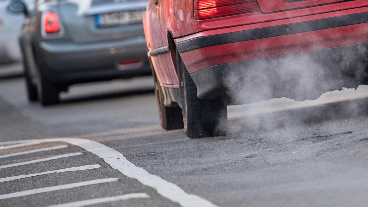 Rückansicht von Autos, die durch die Stadt fahren. Bei hintersten Auto sind die Abgase aus dem Auspuff deutlich zu sehen. Rückansicht von Autos, die durch die Stadt fahren. Bei hintersten Auto sind die Abgase aus dem Auspuff deutlich zu sehen.