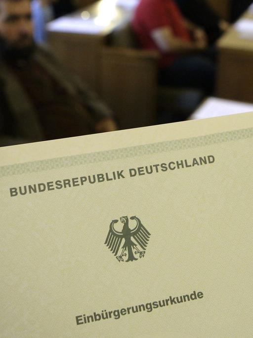 Die Einbürgerungsurkunde der Bundesrepublik Deutschland, im Hintergrund Migranten - aufgenommen bei einer Einbürgerungsfeier.