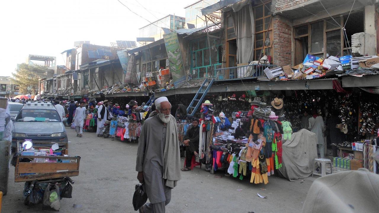Auf der Einkaufsstraße in Khost stehen Händler mit Kleiderständern, die Häuser sehen kaputt und marode aus.