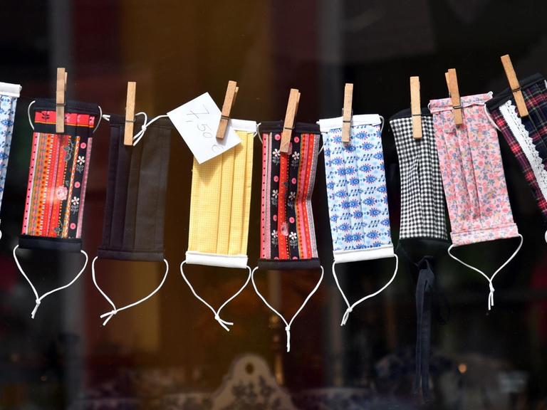 Mund-Nase-Masken zum Schutz vor dem Coronavirus in einem Schaufenster in Erfurt (Thüringen). Die bunt gemusterten Masken sind an einer Wäscheleine aufgehängt.