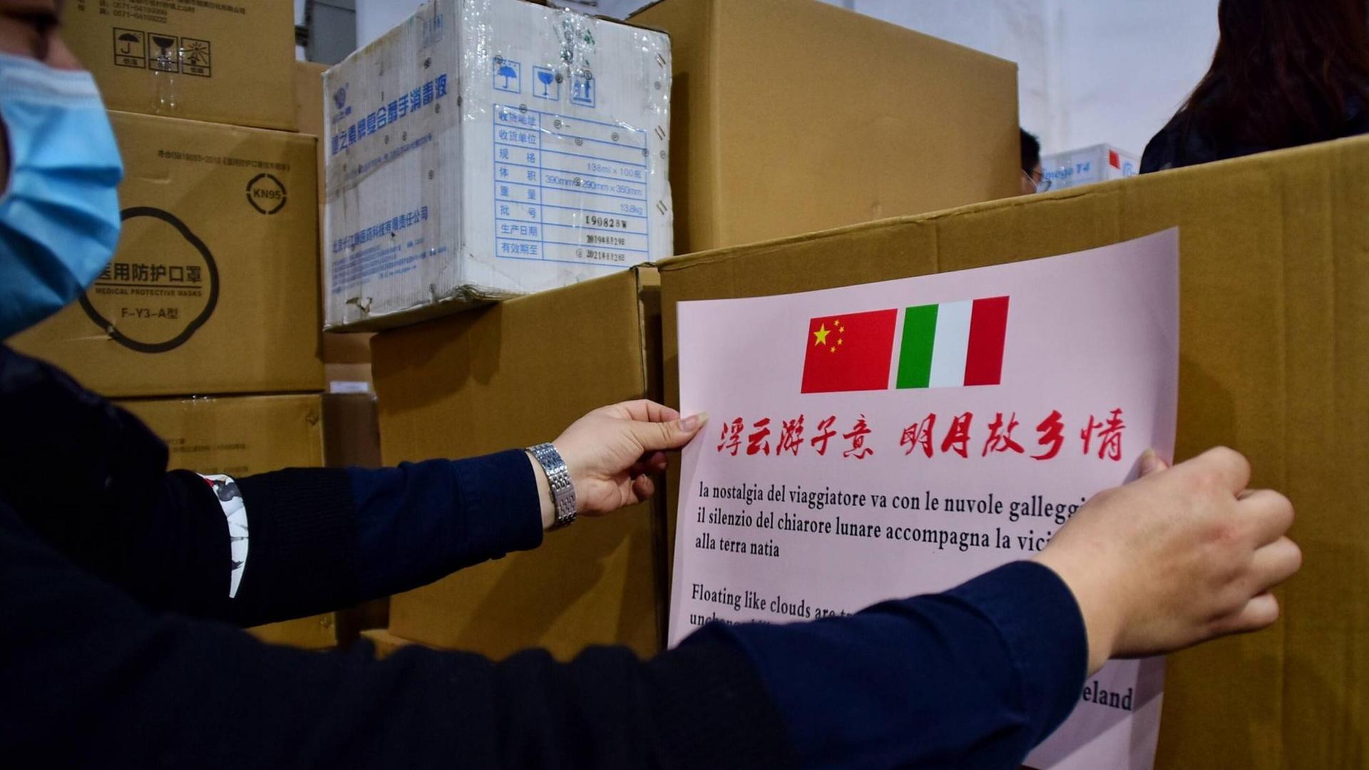 In China wird ein Schild mit einer chinesischen und einer italienischen Flagge auf ein Hilfspaket in der Corona-Krise geklebt. In China wird ein Schild mit einer chinesischen und einer italienischen Flagge auf ein Hilfspaket in der Corona-Krise geklebt.