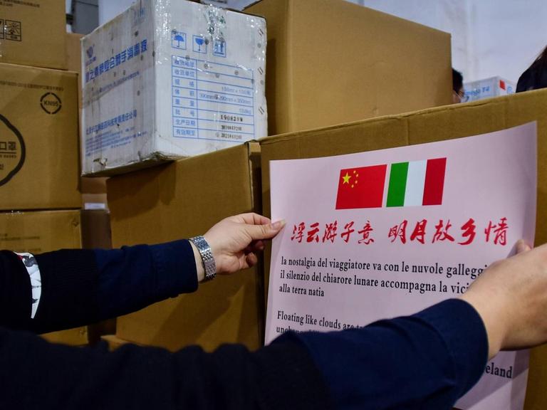 In China wird ein Schild mit einer chinesischen und einer italienischen Flagge auf ein Hilfspaket in der Corona-Krise geklebt.