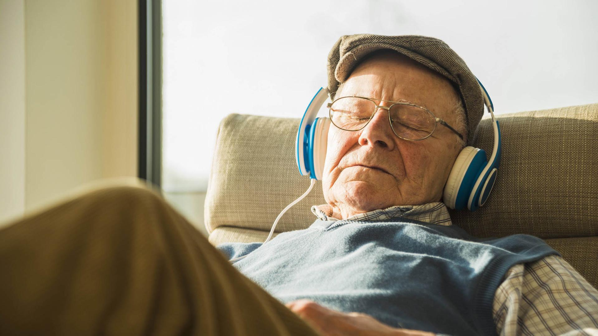 Ein älterer Mann sitzt mit Kopfhörern auf einem Sessel und hört Musik. Ein älterer Mann sitzt mit Kopfhörern auf einem Sessel und hört Musik.