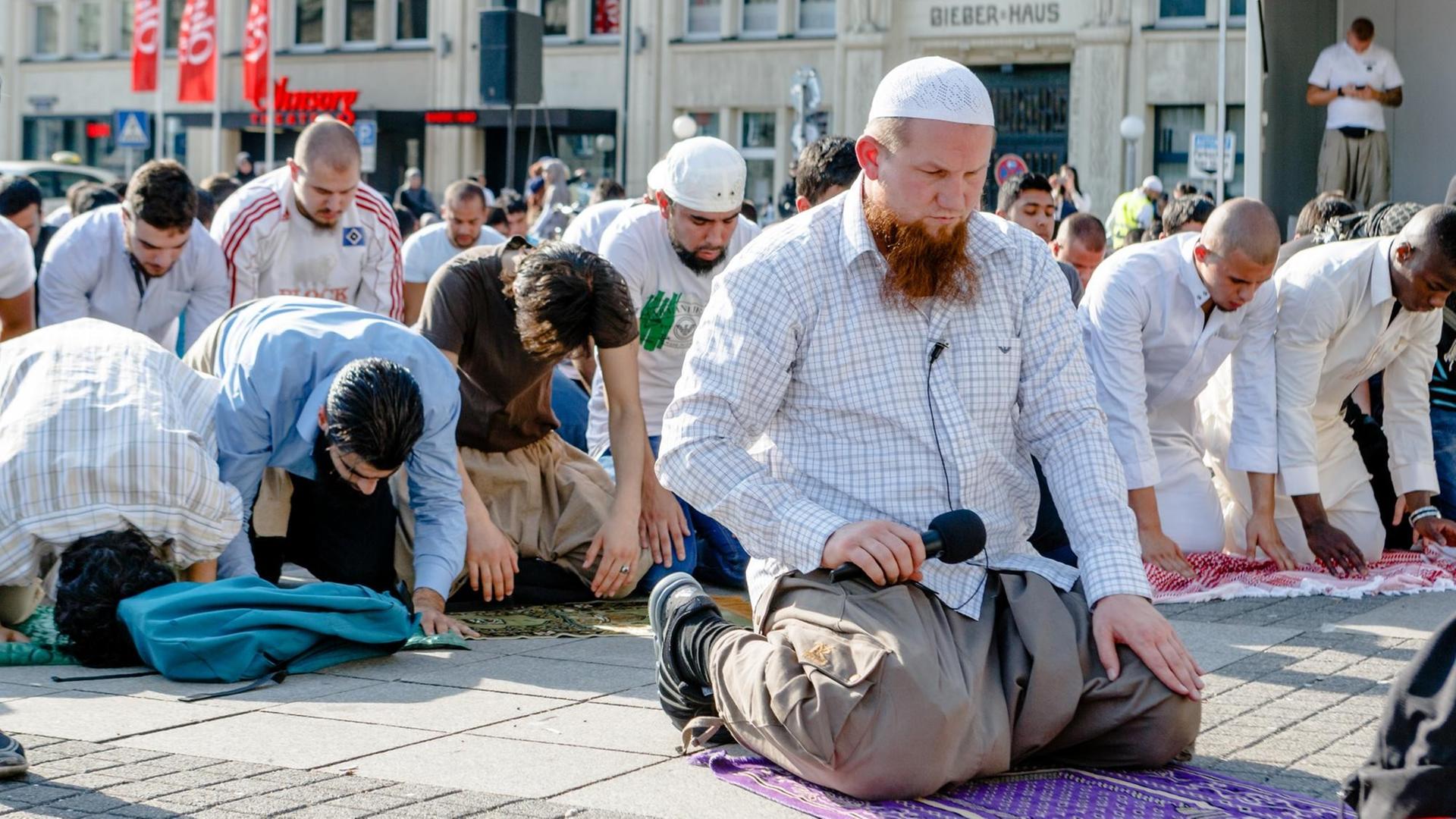 Der salafistische Prediger Pierre Vogel kniet auf dem Boden, hinter ihm beugen sich Dutzende junge Männer betend zu Boden. Der salafistische Prediger Pierre Vogel kniet auf dem Boden, hinter ihm beugen sich Dutzende junge Männer betend zu Boden.